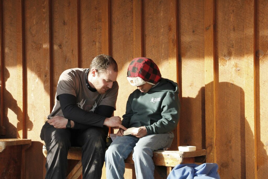camp counselor giving boy advice about his woodcarving